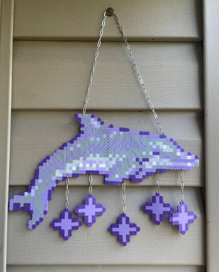 a perler in the shape of ecco the dolphin from a video game of the same name with purple sparkles dangling from chains connected to it