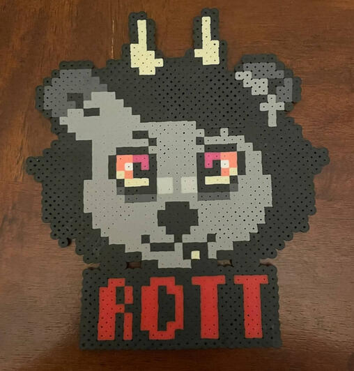 a perler in the shape of a bear fursona with horns and is dark grey with the name Rott displayed in red