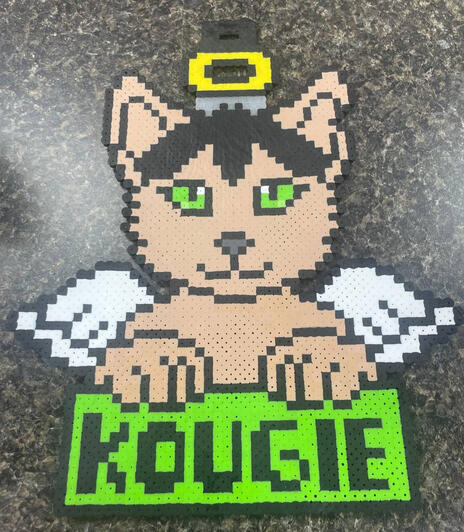 a perler in the shape of a tan cat with angel wings a halo with the name kougie displayed