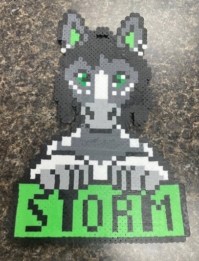 a perler in the shape of a dark grey horse with green eyes with the name storm being displayed on it